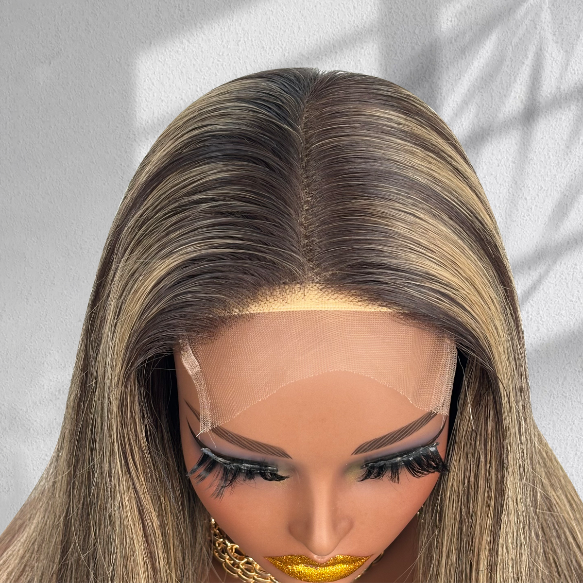 Close-up of the center part and HD lace on a balayage wig with dark brown roots and blonde highlights.