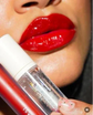 Woman with glossy red lips holding clear lip gloss and red lipstick tube
